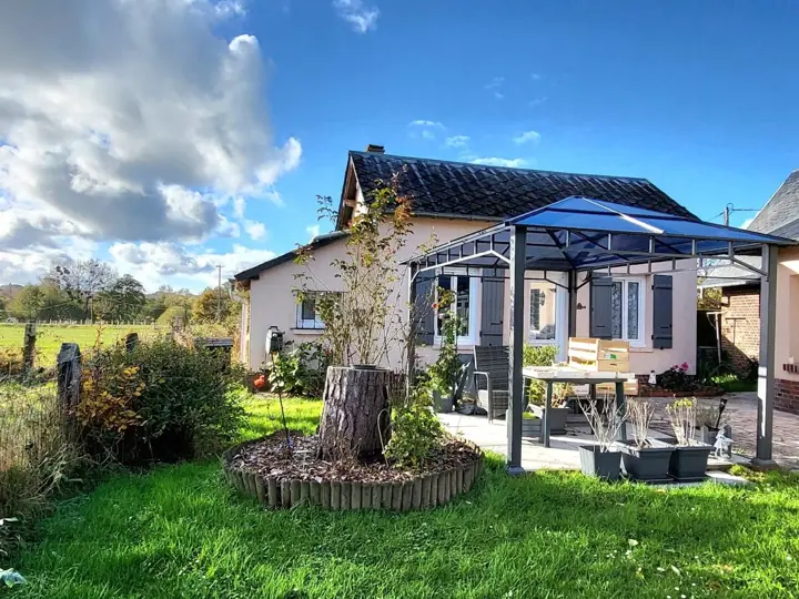 La petite maison aux volets bleus et sa tonnelle au milieu du jardin, sous un ciel bleu
